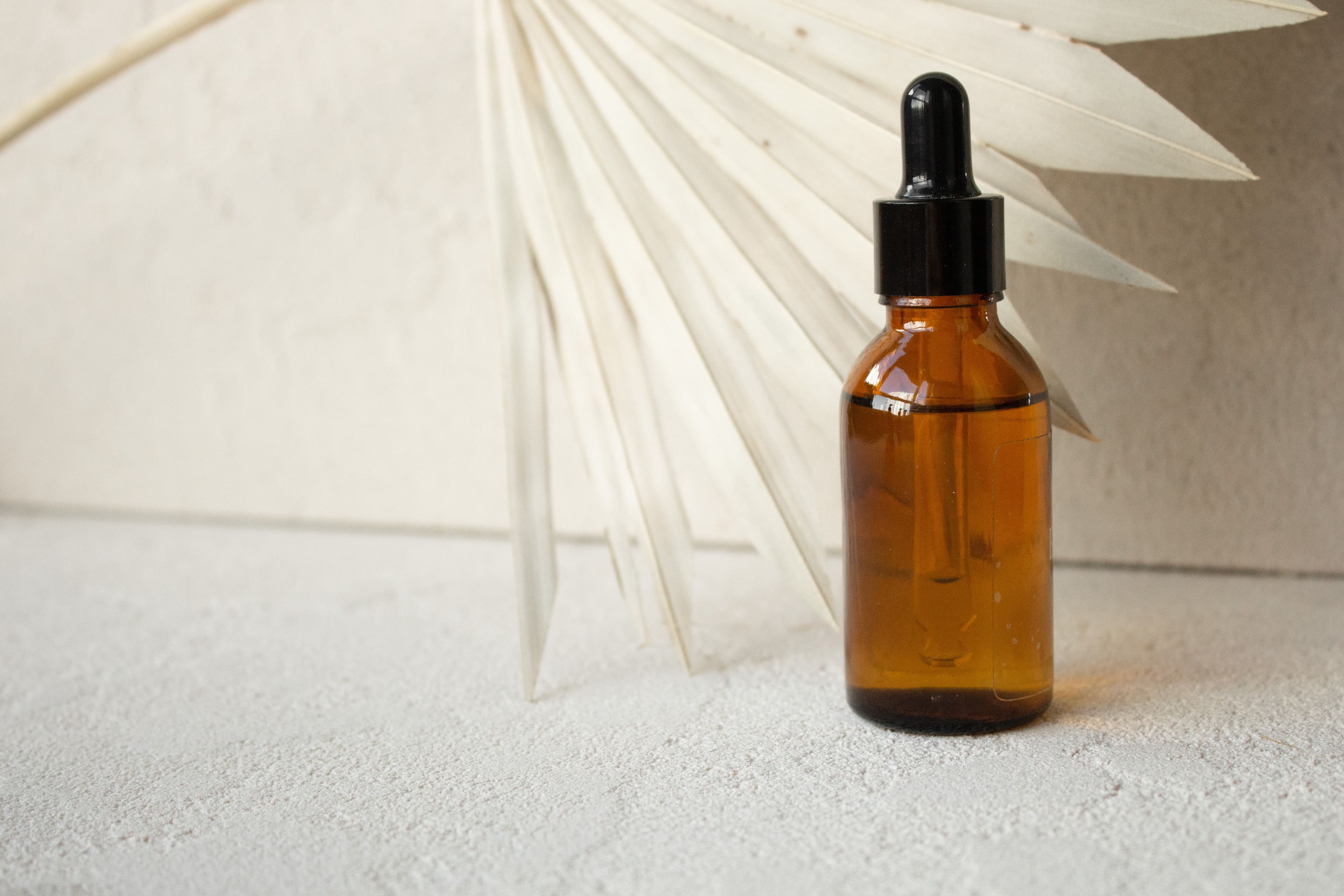 Amber glass dropper bottle beside a dried palm fan leaf on a textured surface.